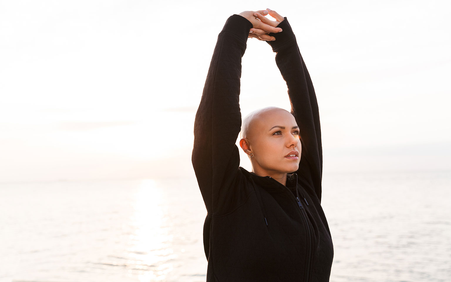 Bald woman doing yoga outdoors for a blog about The Benefits of Exercise and Cancer Treatment