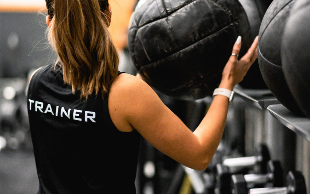 female trainer holding medicine ball in gym for a blog about the benefits of having a personal trainer