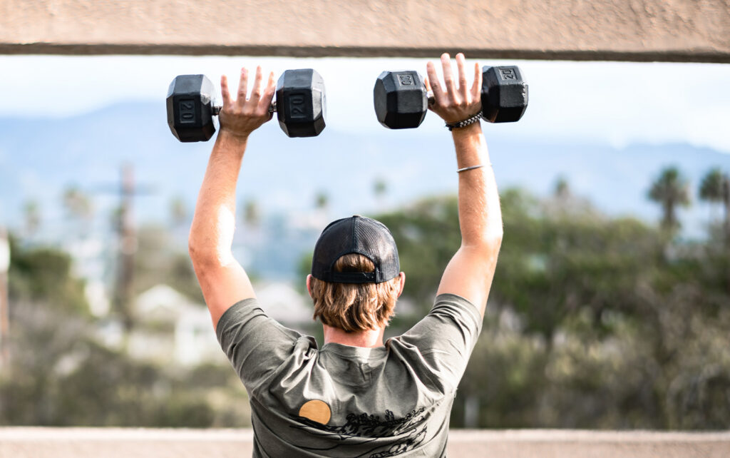 Man lifting dumbbells overhead for a blog about building muscle mass and losing fat