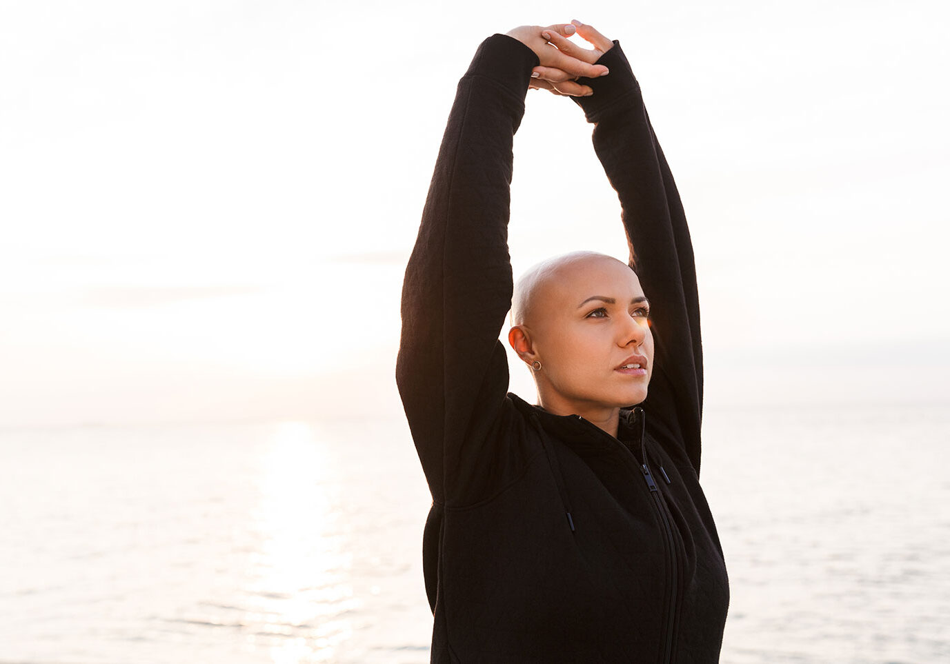 Bald woman doing yoga outdoors for a blog about The Benefits of Exercise and Cancer Treatment