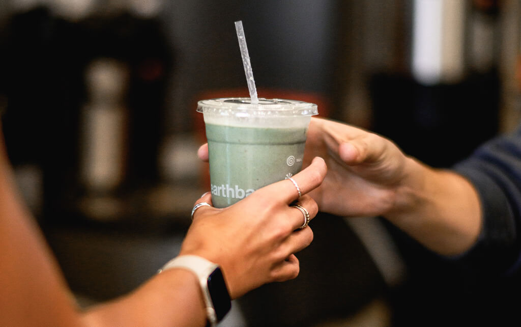 someone handing an earthbar smoothie to someone in celebration of National Green Juice Day